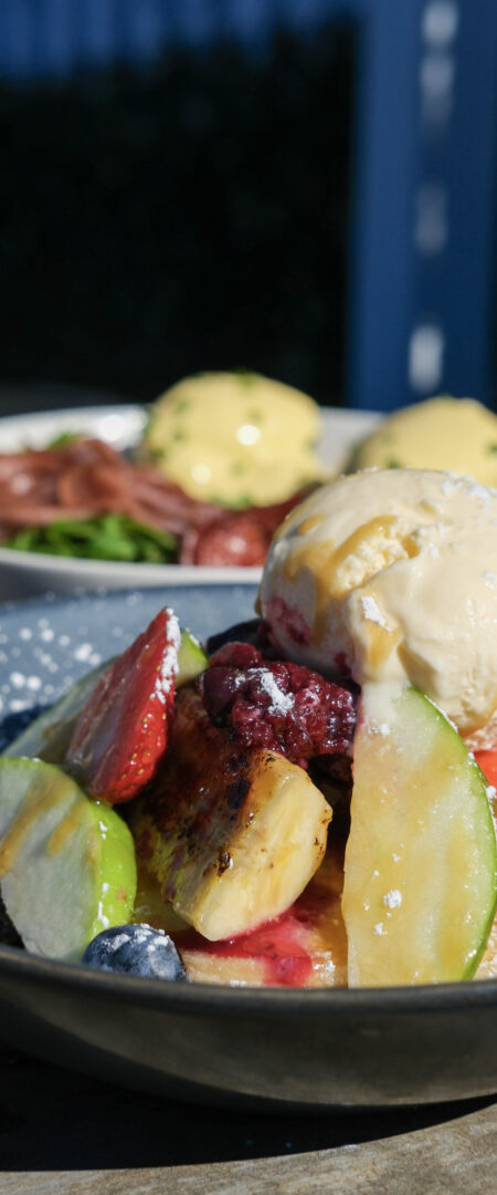 Stack of fluffy pancakes topped with fresh strawberries, blueberries, berry compote, maple syrup and vanilla ice cream at Geographe restaurant in Coles Bay, Tasmania.