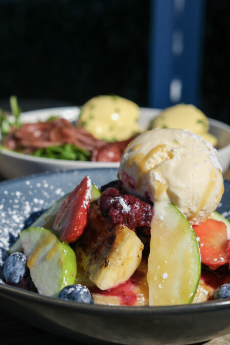 Stack of fluffy pancakes topped with fresh strawberries, blueberries, berry compote, maple syrup and vanilla ice cream at Geographe restaurant in Coles Bay, Tasmania.